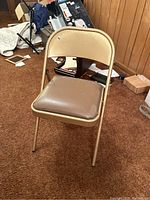 Front view of the beige metal folding chair with padded seat and backrest showing wear and tear.