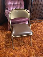 Front view of the metal padded folding chair showing the brown padded seat and backrest with beige metal frame.