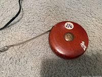 Front view of round wooden tape measure with brass center, showing wear and label 216.