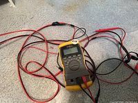 Compact Radio Shack digital multimeter in yellow and black with attached test probes lying on carpet.