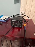 RMSTATOR 939D soldering station on wooden table with soldering iron connected, showing front panel with temperature dial and heating port.