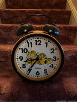 Front angle view of the vintage Sunbeam Garfield twin bell alarm clock showing Garfield on the clock face and two black bells on top.