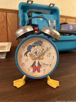 Front view of the vintage twin bell alarm clock featuring Donald Duck graphic on clock face, blue case and yellow duck feet.