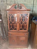 Front view of wooden china cabinet showing decorative glass doors with fretwork and brass handles, drawer, and lower double door cabinet.