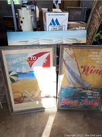 Framed coastal beach and sailboat art prints leaning against wall with other objects in background