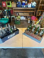 View of two crates on table containing vintage A-Treat glass bottles, one black plastic crate and one wooden crate.