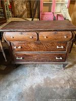 Front view of vintage oak dresser showing four drawers with glass handles, visible wear and tear, and a missing bottom in one top drawer.