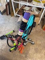 Photo showing two rolled yoga mats with carrying bags, resistance band, tabletop pedal bike, and assorted dumbbells on the floor.