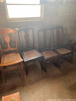Four wooden fiddleback caned chairs lined up including two rockers in natural light by a window in a room with exposed concrete block walls.