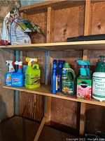 Photo of assorted garden chemical bottles including Miracle-Gro, Flo-master spray bottle, and others on wooden shelf