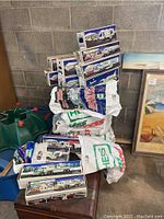 Multiple collectible Hess Christmas trucks stacked and arranged on furniture and bags. Boxes feature various truck models and winter scenes.