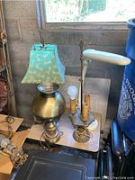 Four lamps displayed together. Includes a brass pump lamp with blue fabric shade, a vintage three bulb metal lamp, and an adjustable office type light.
