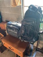 Photo showing vintage leather suitcase at bottom, smaller gray and black carry-on bag to left, and black nylon rolling duffel bag standing upright on right.