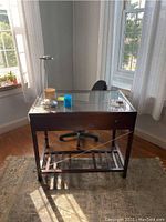 Glass top office desk with wooden frame and lower shelf, keyboard drawer visible, lamp and accessories on top.