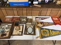 Entire lot laid out on two white tables showing vintage pennants, assorted frames, mirror, framed photos, and many loose photos.