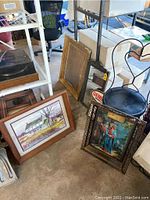 Four items on the floor: a vintage gilded frame mirror, a framed rural house picture, framed illuminated Jesus artwork, and a Genesee beer illuminated calendar partially visible.
