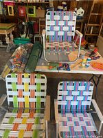 Three folding chairs (two low beach chairs with wooden armrests and one regular height folding chair) with woven multicolor seats and backs, sitting on white table along with additional pool and beach supplies.