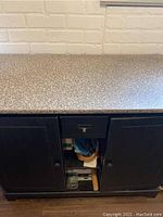 Closed view of wood storage cabinet with faux marble top, two doors, central drawer.