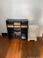 Dark wooden storage unit with baskets and drawers next to small white wooden bookshelf