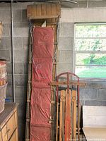 Full view of the 10-foot wood and metal multi-person toboggan with padded red seating leaning against a wall