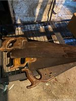 Three wooden-handled wood saws stacked and showing rusted blades on a metal shelf