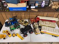 Overall view of all the assorted toy trucks and vehicles on a white table showing positioning and condition.