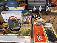 Overview photo showing two electric train sets, Lite-Brite sets, lead soldier set, and boxed dolls on a table.