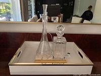 Front view of two crystal decanters with stoppers on white faux leather tray with gold-tone trim