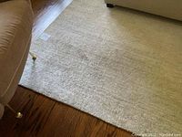 Corner of light grey rug under furniture on hardwood floor