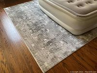 Full view of grey geometric rug installed under an inflatable mattress on wood floor