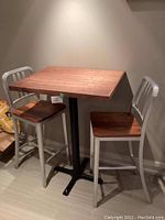 High top table with two matching chairs, showing the wood top and metal base with wood and silver chairs.