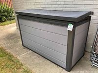 Front left angle view of closed resin storage box against brick wall.