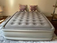 Front view of fully inflated grey Outbound queen air mattress with two pillows on top, placed on a rug in a room.