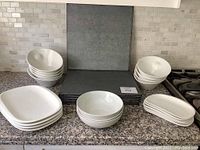 All white ceramic dishes arranged with gray textured placemats stacked upright behind them on countertop