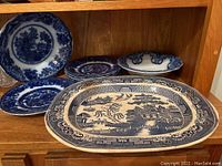Photo showing antique Blue Willow platter and Flow Blue dishes and bowl on wooden shelf