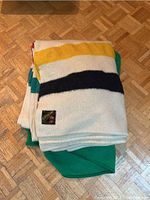 Folded wool blankets stacked on parquet floor showing traditional multicolor stripes.
