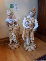 Pair of ceramic figurines depicting a man and woman in period attire, standing on textured bases.
