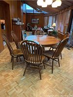 Six chairs arranged around oval dining table on parquet floor in sunroom.