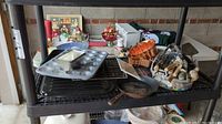 Shelf view showing assorted bakeware including muffin pan, metal baking dishes, cast iron pan, copper cake pans, and container with kitchen utensils