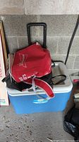 Blue and white Coleman Party Stacker hard cooler with black retractable handle and wheels, with two red backpack style soft coolers on top, one with Budweiser branding.
