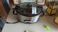 Front angle view of Crockpot original slow cooker showing stainless steel body, black handles, and glass lid with black handle on countertop.