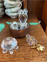 Crystal figurines displayed on wooden shelf, including owl with small bird on wooden base, turtle figurine, small frog with gold-tone feet, and other clear crystal decorative items.