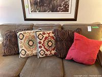 Five cushions arranged on a beige couch, showing mix of patterns and colors.