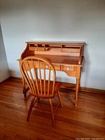 Front view of the pine wood desk with chair showing the hutch with compartments and drawers, desk surface, and spindle back chair.