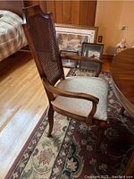 Captain's chair with armrests, cane back, and upholstered seat shown on a floral patterned rug and wood floor