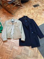 Two jackets laid flat on a parquet floor: beige Roots leather jacket and navy blue pea coat.