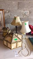 Photo showing two table lamps and two hanging glass light fixtures grouped on tabletop against rough wall background.