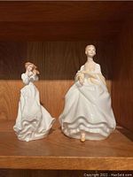 Two Royal Doulton porcelain figurines on shelf showing overall size and form
