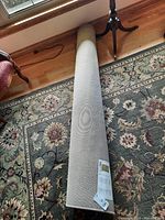 Rolled beige Ikea Vium rug placed on a larger patterned carpet, showing the label and tag attached to the rug.