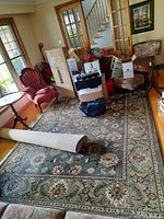 Full view of the area rug in a room with furniture and boxes on top of it, showing the floral pattern and color scheme.